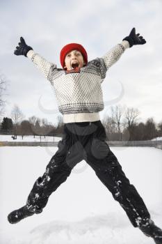 Royalty Free Photo of an Excited Boy Wearing a Sweater and Red Winter Cap Jumping in the Air With Arms and Legs Outstretched