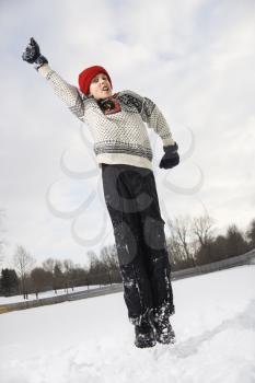Caucasian boy wearing sweater and red winter cap jumping in air with arm outstretched.