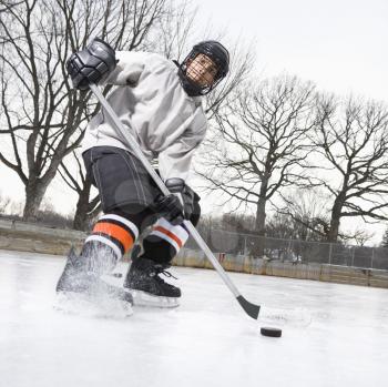 Royalty Free Photo of a Boy in an Ice Hockey Uniform Skating on an Ice Rink Moving a Puck