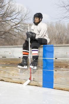 Royalty Free Photo of a Boy in an Ice Hockey Uniform Holding a Hockey Stick Sitting on the Sidelines