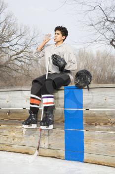 Royalty Free Photo of a Boy in an Ice Hockey Uniform Sitting on the Sidelines Drinking Water