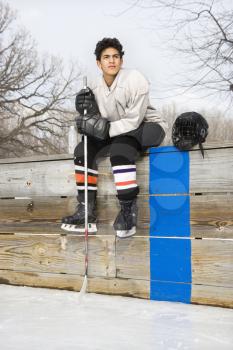 Royalty Free Photo of Boy in an Ice Hockey Uniform Holding a Hockey Stick Sitting on the Sidelines