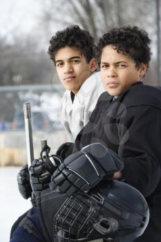 Royalty Free Photo of Two Boys in Ice Hockey Uniforms Holding a Hockey Sticks Sitting on the Sidelines