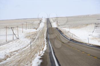 Royalty Free Photo of a Road Over a Rolling Hill Landscape With Snow and Power Lines