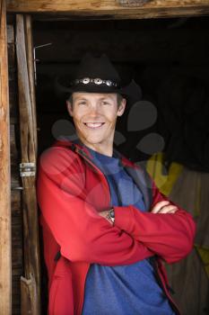 Royalty Free Photo of a Young Man Wearing a Cowboy Hat Leaning in a Doorway Smiling