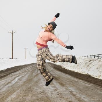 Royalty Free Photo of a Woman in Winter Clothes Standing on a Muddy Dirt Road Jumping and Smiling