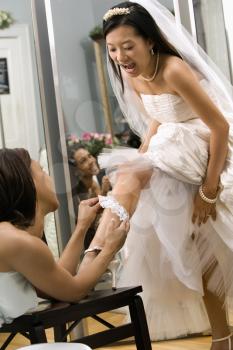 Royalty Free Photo of an African-American Bridesmaid Placing a Garter on a Bride's Leg