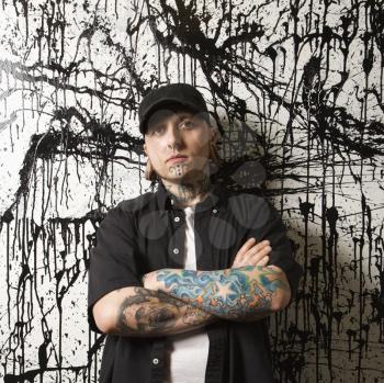 Royalty Free Photo of a Tattooed and Pierced Man Standing Against a Paint Splattered Background