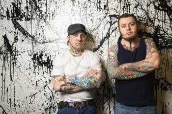 Royalty Free Photo of Tattooed Men Leaning Against a Paint Splattered Wall