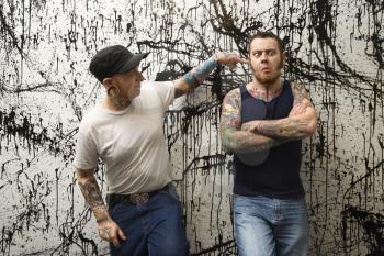 Royalty Free Photo of Two Tattooed Men Standing Against a Paint Splattered Background