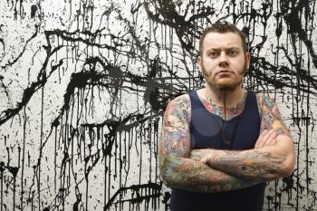 Royalty Free Photo of a Tattooed Man Leaning Against a Paint Splattered Wall