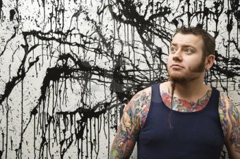 Royalty Free Photo of a Tattooed Man With a Braided Beard Standing Against a Paint Splattered Background