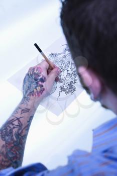 Royalty Free Photo of a Male Tattoo Artist Drawing a Tattoo on a Light Table