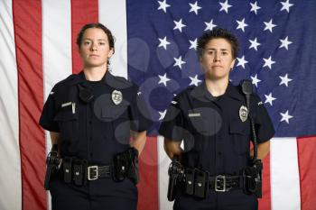 Royalty Free Photo of Policewomen Standing With Arms Behind Their Backs and American Flag as a Backdrop