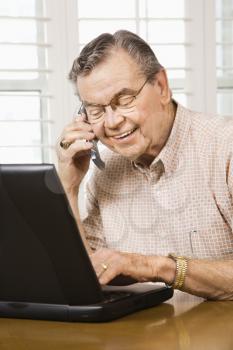 Royalty Free Photo of an Older Man Typing on a Laptop and Talking on a Cellphone