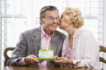 Royalty Free Photo of an Older Woman Kissing Her Husband While Holding a Birthday Cake