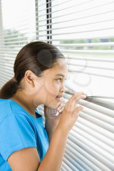 Royalty Free Photo of a Preteen Girl Looking Through the Blinds While Talking on a Cellphone