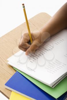 Royalty Free Photo of a Girl at a School Desk Writing in a Notebook With Pencil