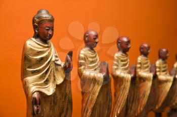 Royalty Free Photo of Wooden Statues of Buddha With Disciples Against an Orange Wall