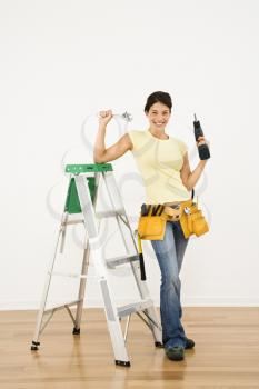 Royalty Free Photo of a Woman Standing at Home With a Ladder and Holding Tools Smiling