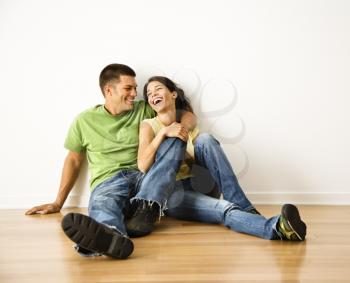 Royalty Free Photo of an Attractive Couple Sitting Together on Hardwood Floor in Home Smiling and Laughing