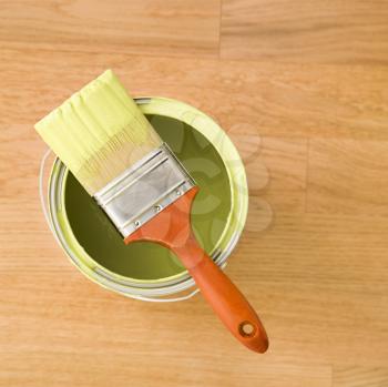 Royalty Free Photo of a Paintbrush Resting on a Paint Can on a Wood Floor