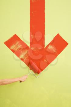 Royalty Free Photo of a Hand Painting a Red Downwards Arrow on a Wall