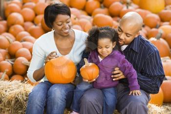 Royalty Free Photo of a Family Sitting on Hay Bales and Holding Pumpkins at an Outdoor Market