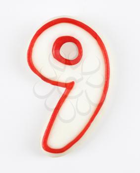 Sugar cookie in the shape of a number nine outlined in red icing.