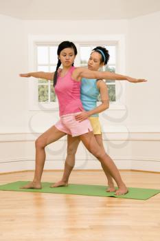 Royalty Free Photo of a Woman Helping Another Woman With Positioning on Her Yoga Pose