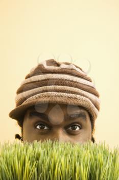Royalty Free Photo of an African-American Man Wearing a Knit Hat with Brim Peeking at Viewer from Behind the Grass