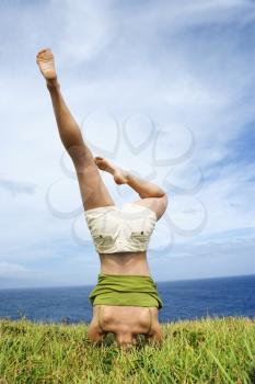Royalty Free Photo of a Young Woman Doing a Headstand With Legs Askew in Grass Near Ocean in Maui, Hawaii