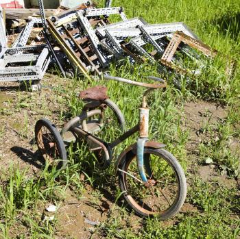 Royalty Free Photo of an Old Abandoned Tricycle in a Grassy Field Next to a Junk Pile