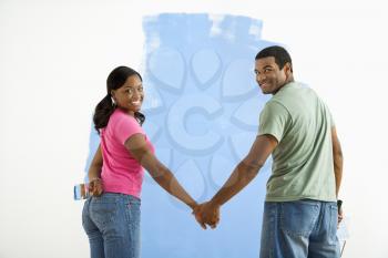 Royalty Free Photo of a Couple Standing Together in Front of a Half-Painted Wall Smiling 