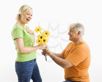 Royalty Free Photo of a Man on Bended Knee Giving a Woman a Bouquet of Yellow Flowers