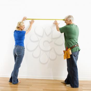 Middle-aged couple measuring wall with tape.