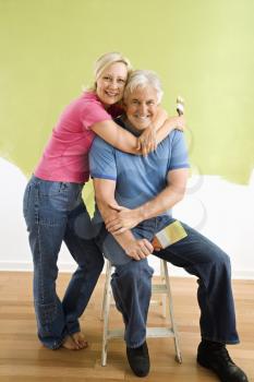 Royalty Free Photo of a Portrait of a Smiling Couple Sitting in Front of a Half-Painted Wall With Paintbrushes