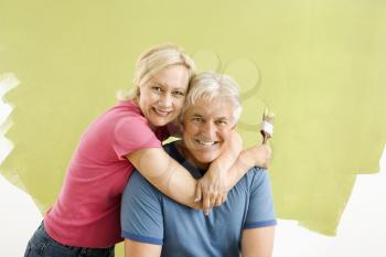 Royalty Free Photo of a Smiling Couple Sitting in Front of a Half-Painted Wall With Paintbrushes