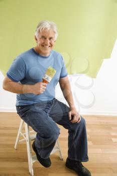 Royalty Free Photo of a Man Sitting in Front of a Half-painted Wall With a Paintbrush