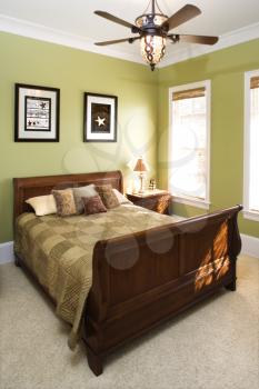 Sleigh bed in a green bedroom with a ceiling fan and wall art. Vertical shot.