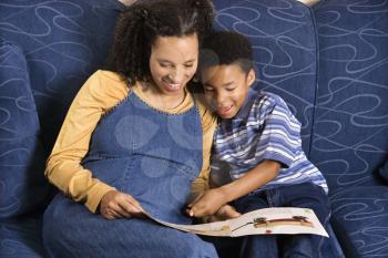 A mid adult woman sitting on a couch reading a book to her young son. Horizontal shot.