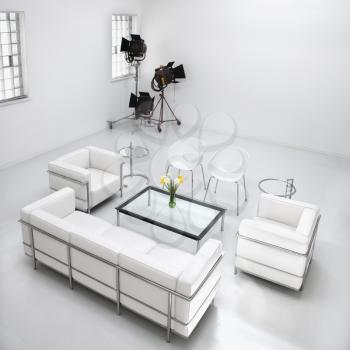 White living room furniture in a white photography studio with commercial lighting in the corner. Square format.