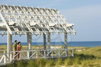 Man and woman look out at the ocean while standing under an arbor. Horizontal shot.