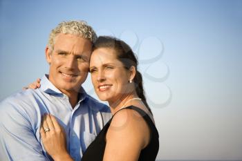 Attractive married couple hug and smile with a blue sky in the background. Horizontal shot.