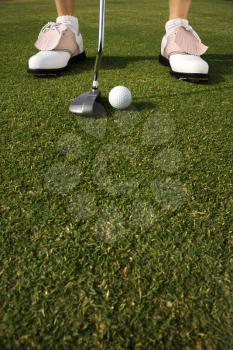 Closeup of a golf ball and the shoes of a golfer about to putt. Vertical shot.