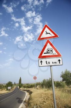 Low angle view of rural road signs and surrounding countryside in Europe. Vertical shot.