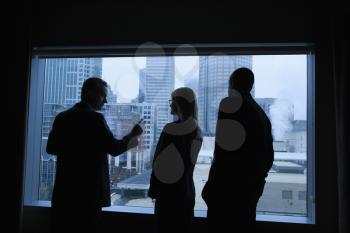 Businesspeople silhouetted in front of a large window that overlooks the city. Horizontal shot.