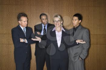 Caucasian businesswoman stands smiling with her hands out as businessmen look at her disapprovingly. Horizontal shot.