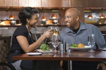 African-American couple dining out. They are toasting with glasses of white wine and smiling. Horizontal shot.