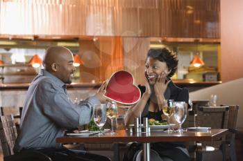 African-American gives a Valentine Day heart box to a surprised woman at a restaurant. Horizontal shot.